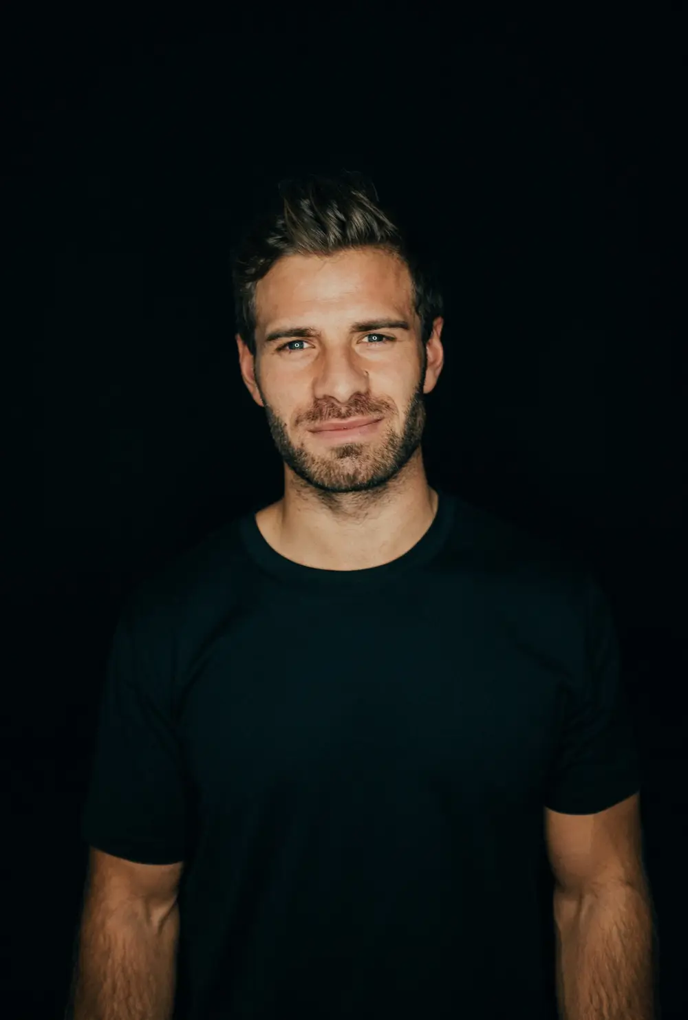 Portrait eines Mannes in schwarzem T-Shirt vor schwarzem Hintergrund